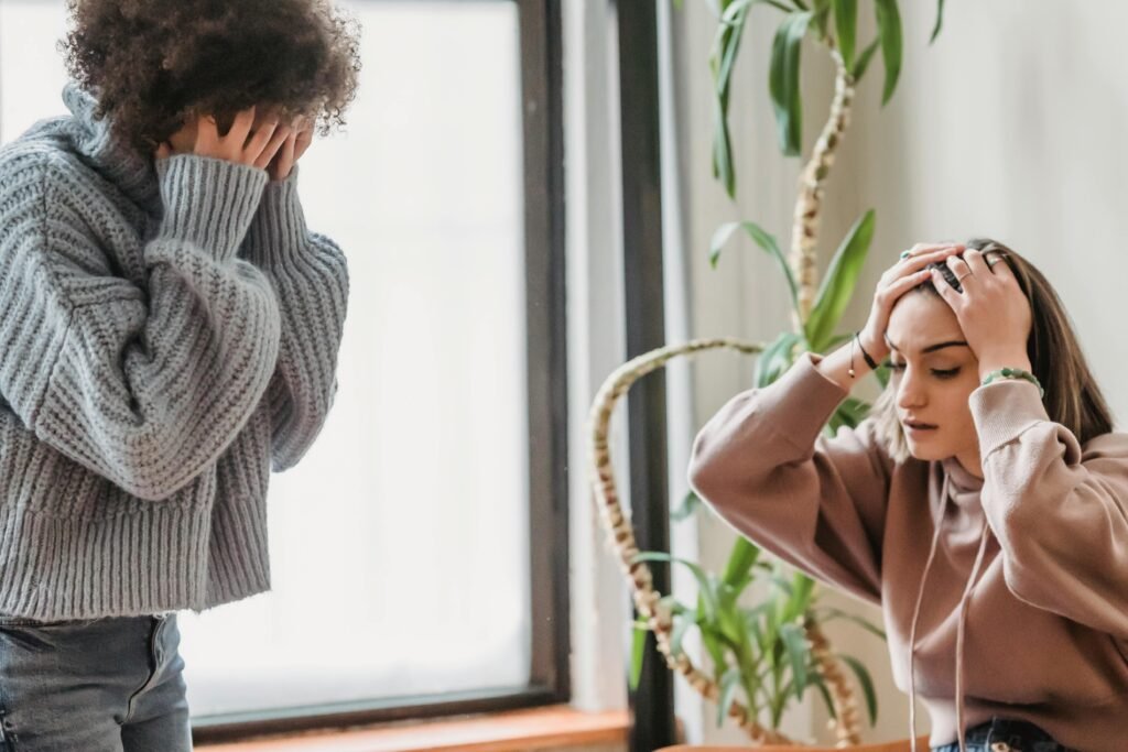 Anonymous female covering face with hands while standing in light room with sad female touching head during conflict at home